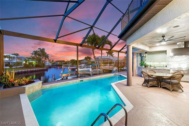 pool at dusk with a lanai, a patio area, ceiling fan, and a water view