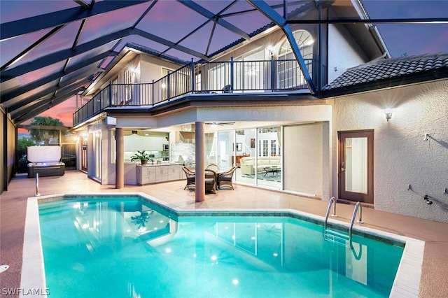 pool at dusk with glass enclosure and a patio area