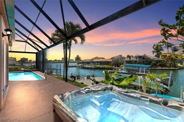 pool at dusk with glass enclosure, a water view, a hot tub, and a boat dock