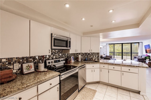 kitchen with white cabinets, stainless steel appliances, kitchen peninsula, and light stone counters