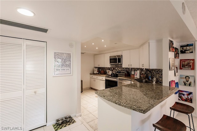 kitchen featuring a kitchen breakfast bar, stainless steel appliances, light tile flooring, tasteful backsplash, and white cabinetry