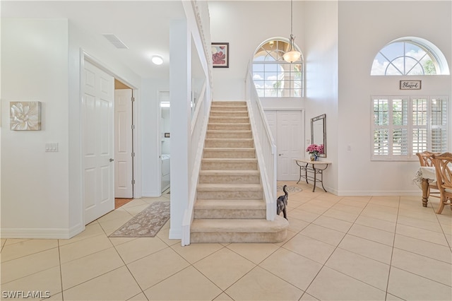 foyer with light tile flooring, a chandelier, and a high ceiling