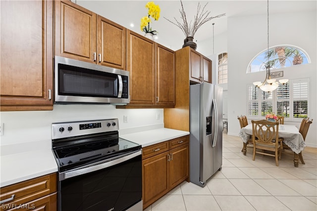 kitchen with stainless steel appliances, light tile floors, decorative light fixtures, a towering ceiling, and an inviting chandelier