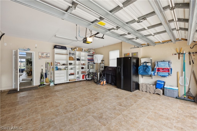 garage featuring a garage door opener and black fridge with ice dispenser