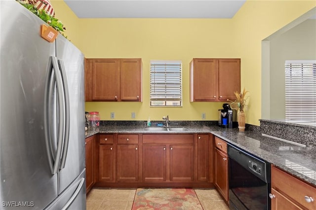 kitchen featuring stainless steel refrigerator, dishwasher, sink, dark stone countertops, and light tile patterned floors