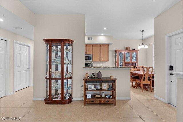 kitchen featuring light stone countertops, light tile patterned floors, light brown cabinets, an inviting chandelier, and hanging light fixtures