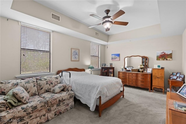 bedroom with light colored carpet, a raised ceiling, and ceiling fan