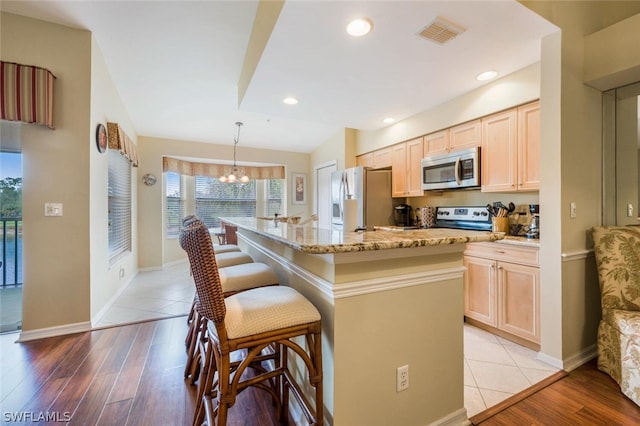 kitchen with an island with sink, hanging light fixtures, light hardwood / wood-style floors, stainless steel appliances, and a notable chandelier