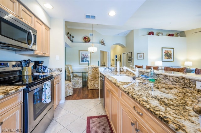 kitchen with light stone countertops, hanging light fixtures, sink, stainless steel appliances, and light tile floors