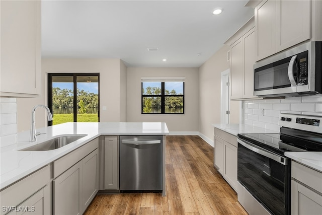 kitchen with light hardwood / wood-style flooring, backsplash, stainless steel appliances, sink, and light stone countertops