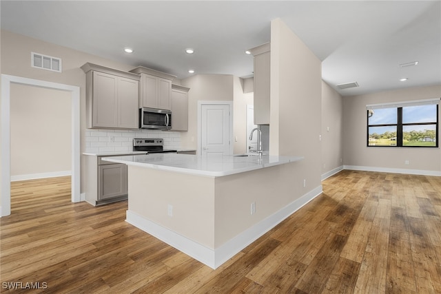 kitchen featuring tasteful backsplash, kitchen peninsula, sink, appliances with stainless steel finishes, and light hardwood / wood-style floors