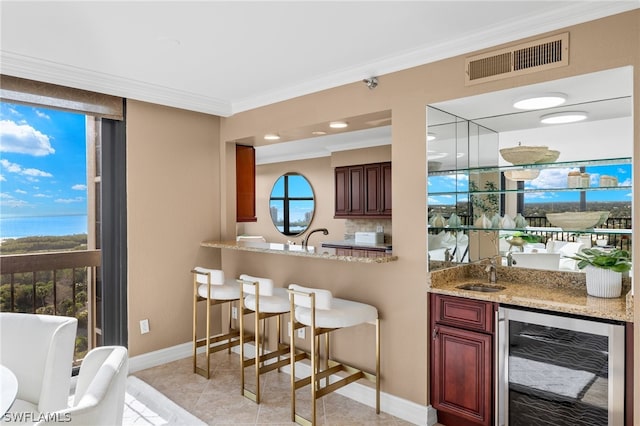 bar featuring light tile floors, light stone countertops, beverage cooler, crown molding, and a water view