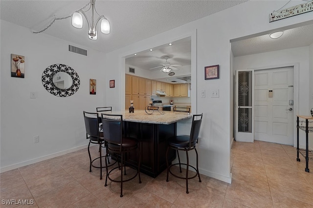 kitchen with light tile patterned flooring, electric range oven, a textured ceiling, decorative light fixtures, and a breakfast bar