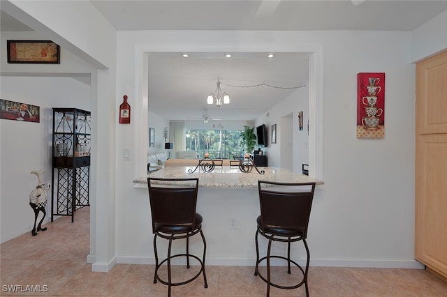 kitchen with a notable chandelier, a textured ceiling, light brown cabinetry, and a breakfast bar area