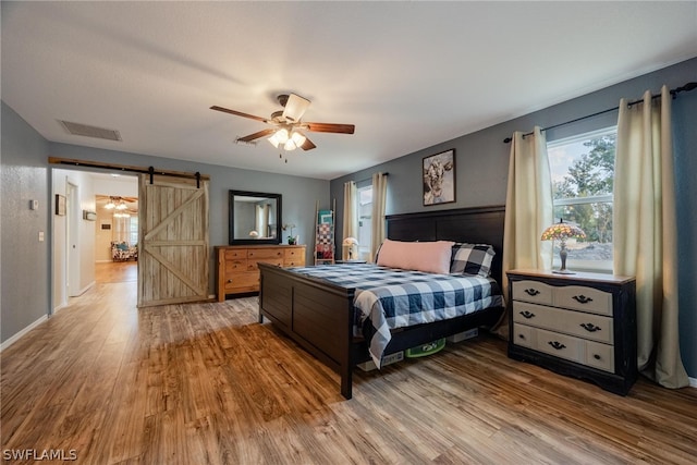 bedroom featuring a barn door, hardwood / wood-style floors, and ceiling fan