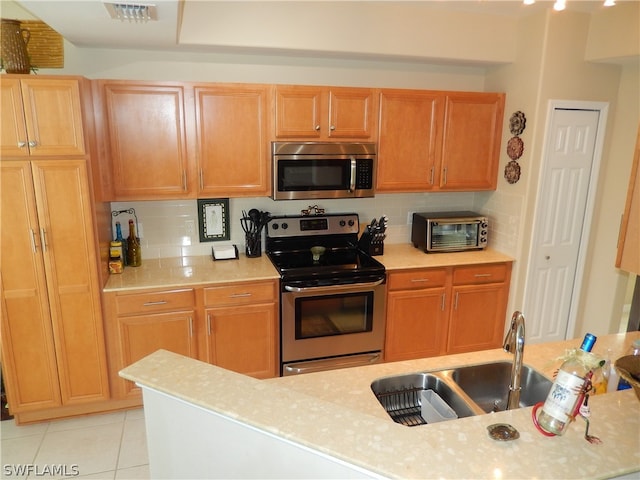 kitchen with appliances with stainless steel finishes, backsplash, sink, and light tile patterned floors