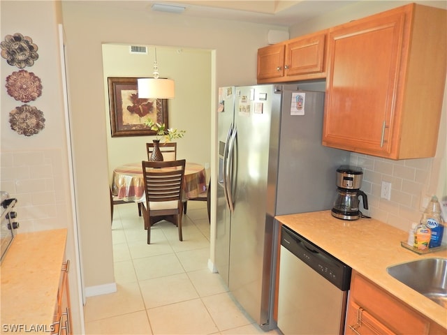 kitchen with sink, light tile patterned flooring, tasteful backsplash, hanging light fixtures, and appliances with stainless steel finishes