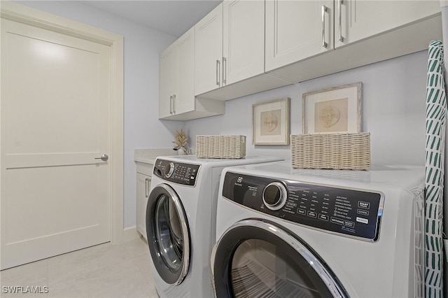 laundry area featuring washing machine and dryer, light tile patterned floors, and cabinets