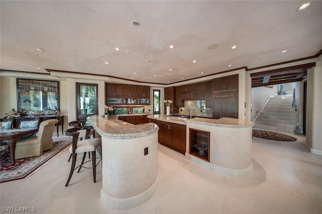 kitchen with ornamental molding, light stone counters, dark brown cabinets, and a large island