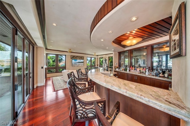 bar with light stone countertops, french doors, and dark wood-type flooring