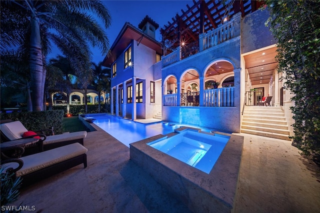 pool at night with a patio area and an in ground hot tub