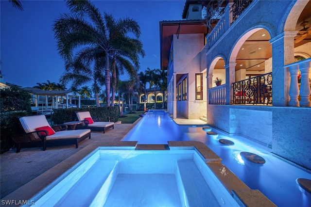 pool at night featuring an in ground hot tub and a patio