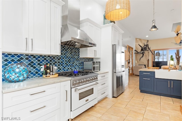 kitchen with stainless steel appliances, blue cabinets, wall chimney range hood, white cabinetry, and hanging light fixtures