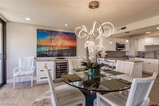 dining room with a chandelier, sink, wine cooler, and light hardwood / wood-style flooring