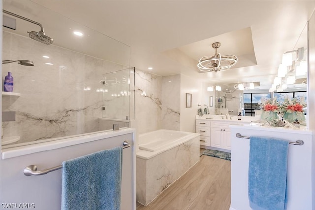 bathroom with an inviting chandelier, a raised ceiling, shower with separate bathtub, vanity, and hardwood / wood-style flooring