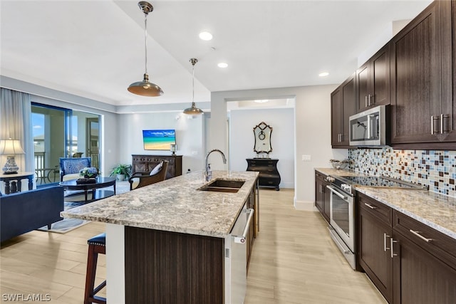 kitchen with sink, a kitchen breakfast bar, hanging light fixtures, stainless steel appliances, and a center island with sink