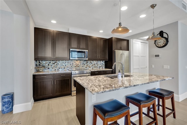 kitchen with appliances with stainless steel finishes, hanging light fixtures, a kitchen island with sink, and a breakfast bar area