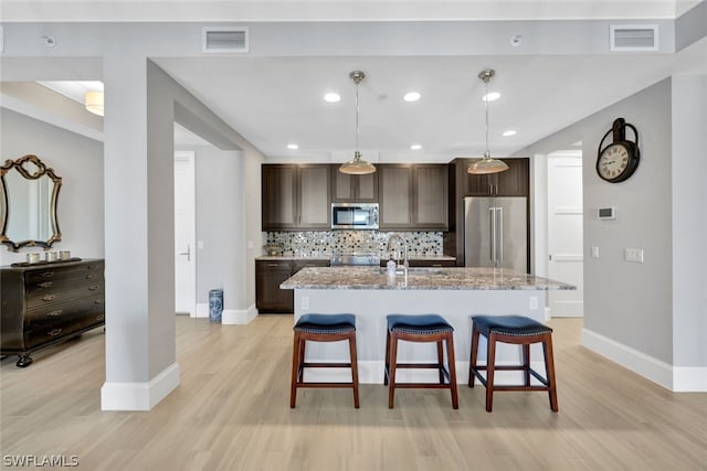 kitchen featuring tasteful backsplash, stainless steel appliances, an island with sink, light stone counters, and a kitchen bar