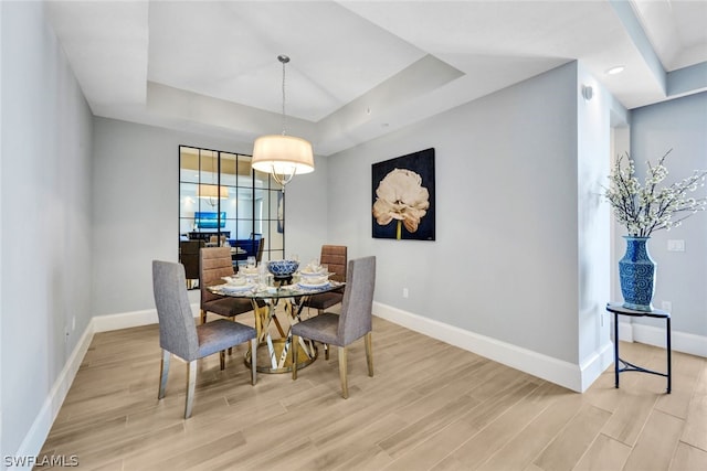 dining space featuring light wood-type flooring and a raised ceiling