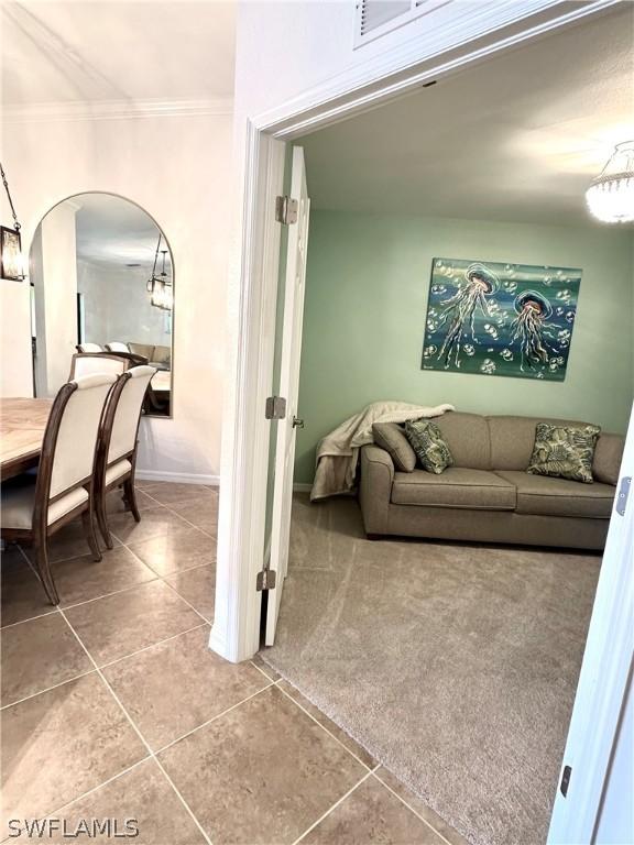 carpeted living room featuring baseboards, arched walkways, crown molding, and tile patterned flooring