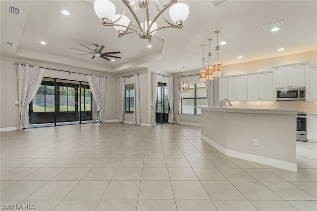 interior space featuring a raised ceiling, stainless steel appliances, pendant lighting, and light stone counters