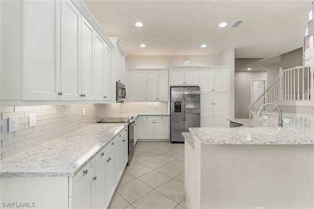 kitchen with white cabinets, backsplash, light stone countertops, and stainless steel appliances