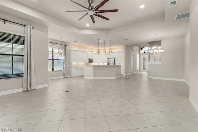 unfurnished living room with light tile floors, a tray ceiling, and ceiling fan with notable chandelier