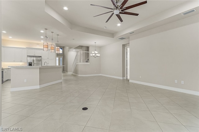 unfurnished living room featuring a raised ceiling, light tile floors, sink, and ceiling fan with notable chandelier