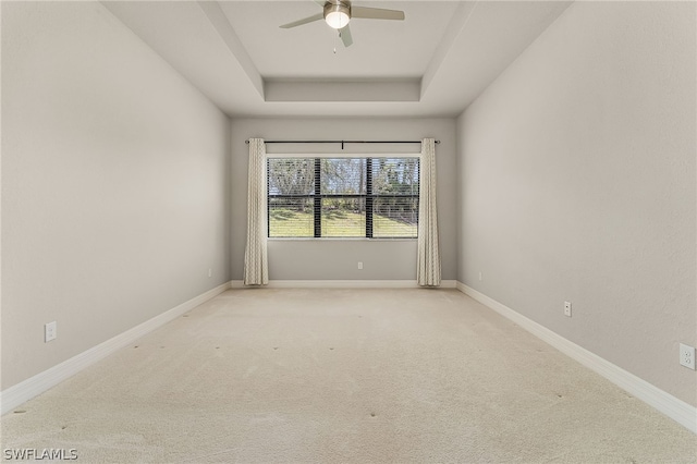 carpeted spare room with a raised ceiling and ceiling fan