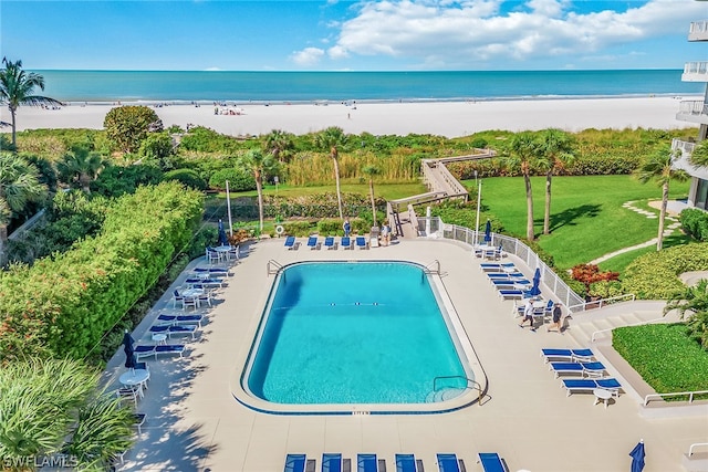 view of swimming pool with a water view, a yard, and a beach view