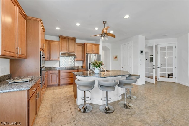 kitchen with appliances with stainless steel finishes, dark stone counters, tasteful backsplash, an island with sink, and a breakfast bar