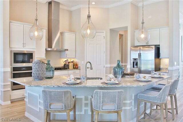 kitchen with decorative light fixtures, an island with sink, stainless steel appliances, wall chimney exhaust hood, and a breakfast bar area