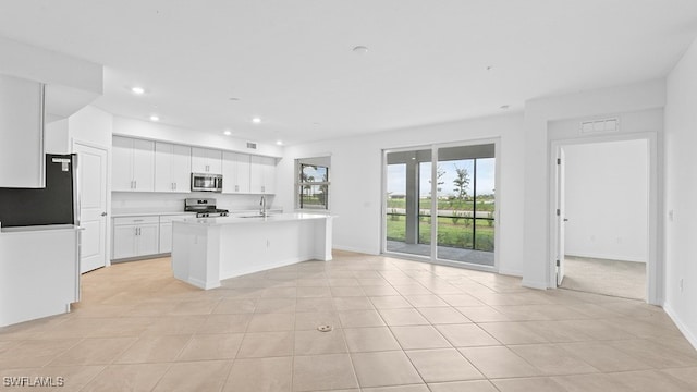 kitchen with light tile patterned floors, appliances with stainless steel finishes, white cabinets, a center island with sink, and sink