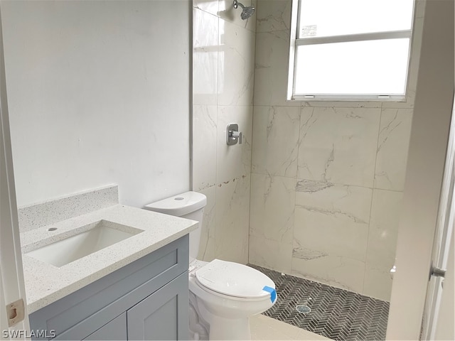 bathroom with tiled shower, vanity, toilet, and tile patterned flooring