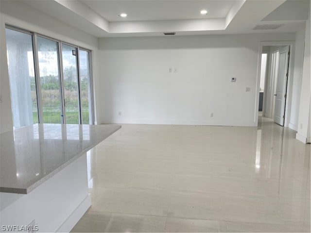 empty room with a raised ceiling and light tile patterned flooring