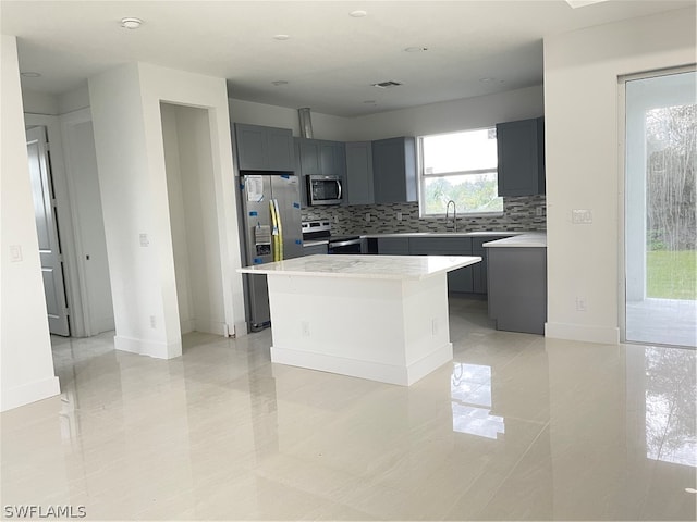 kitchen with a kitchen island, light tile patterned floors, backsplash, stainless steel appliances, and gray cabinets