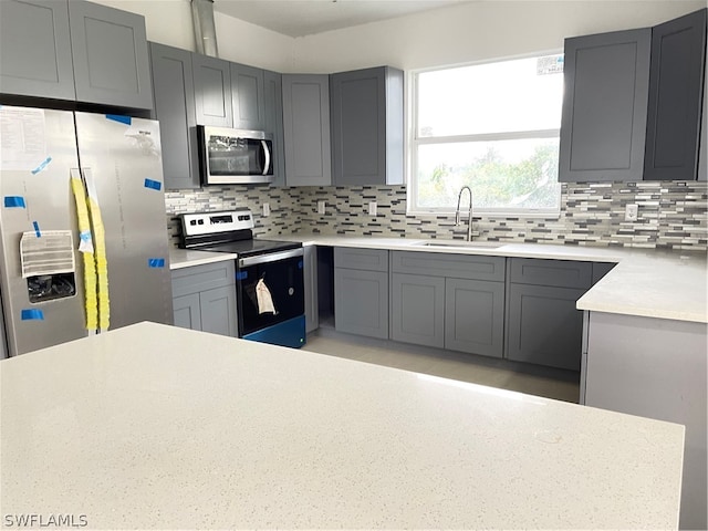 kitchen with gray cabinetry, appliances with stainless steel finishes, backsplash, and sink