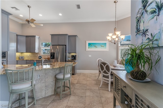 kitchen featuring pendant lighting, stainless steel fridge with ice dispenser, gray cabinetry, backsplash, and ceiling fan with notable chandelier