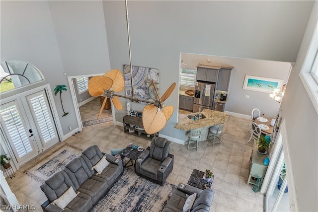 living room featuring light tile floors, a notable chandelier, french doors, and a high ceiling