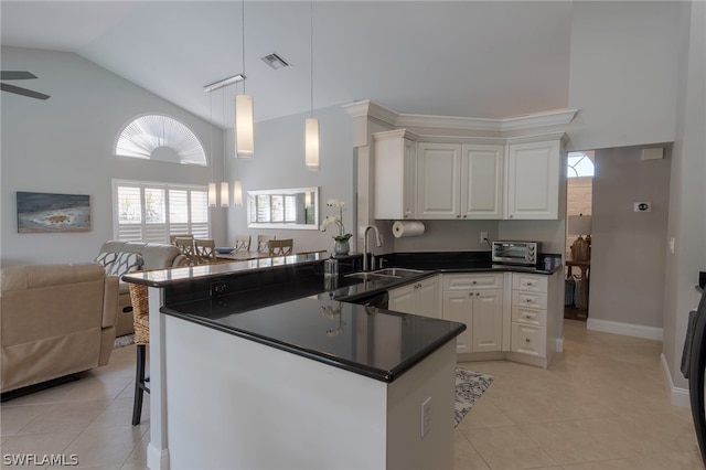 kitchen with light tile patterned flooring, kitchen peninsula, decorative light fixtures, sink, and high vaulted ceiling